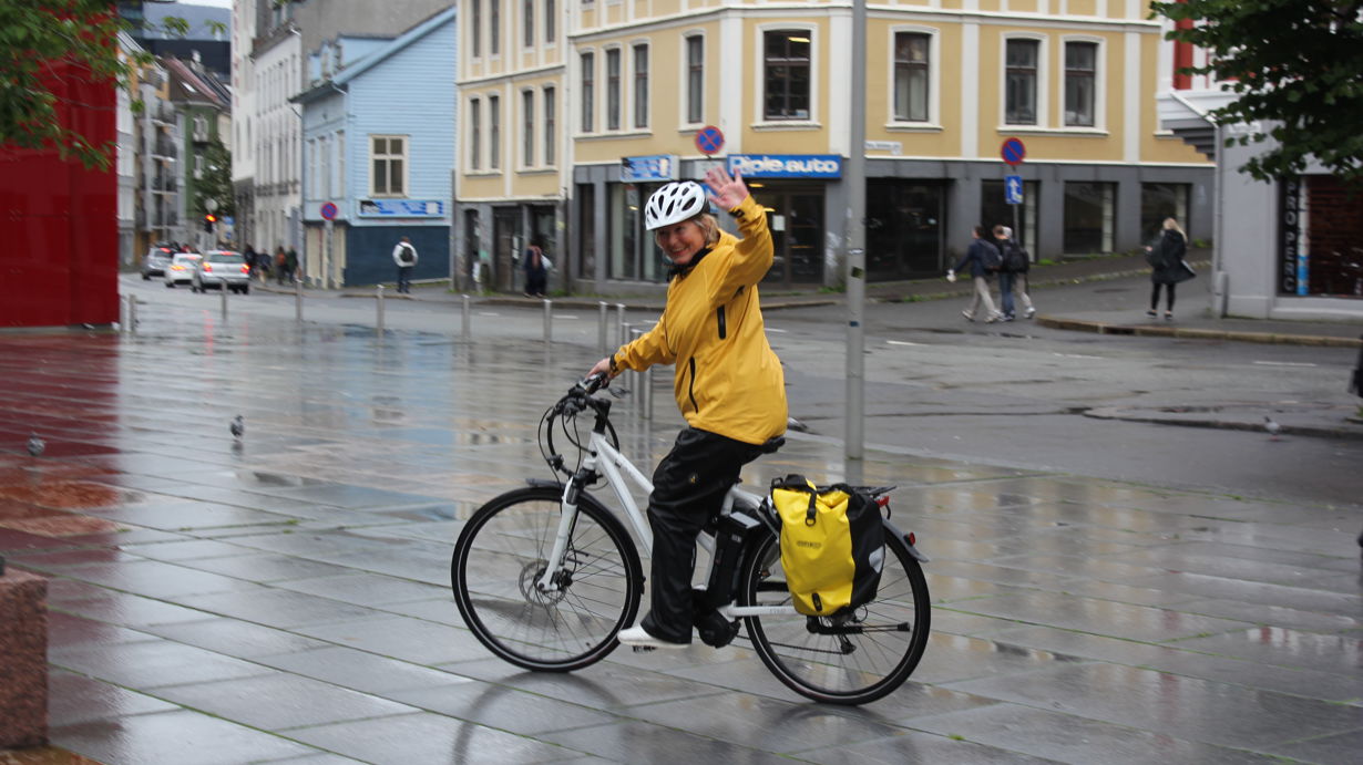 kvinnelig helsefagarbeider på elsykkel vinker mot kamera