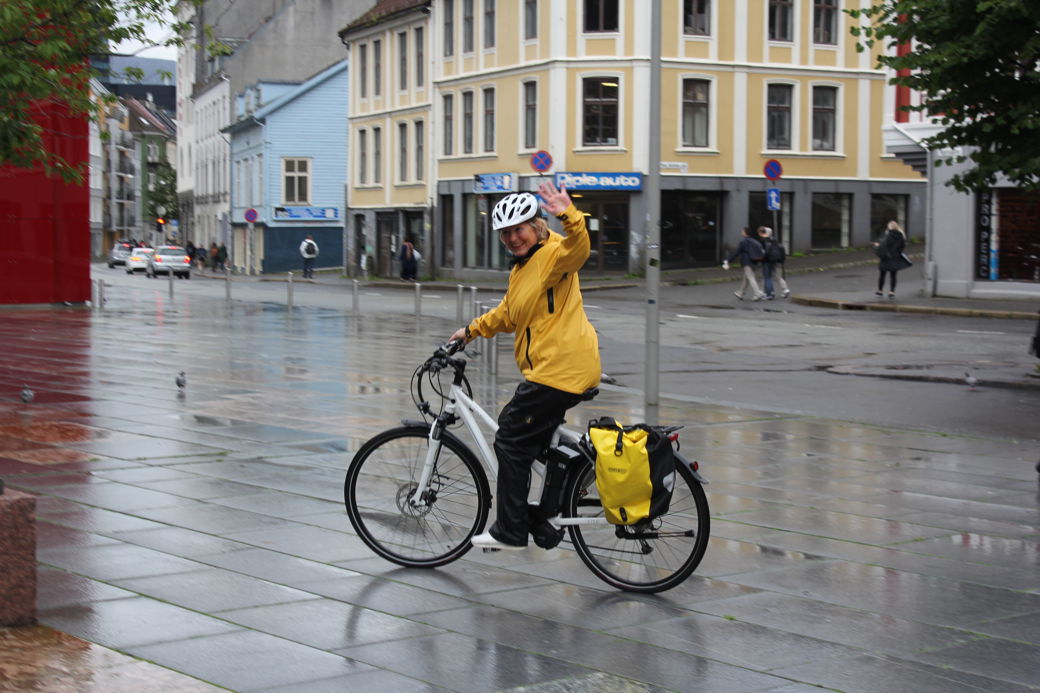 kvinnelig helsefagarbeider på elsykkel vinker mot kamera