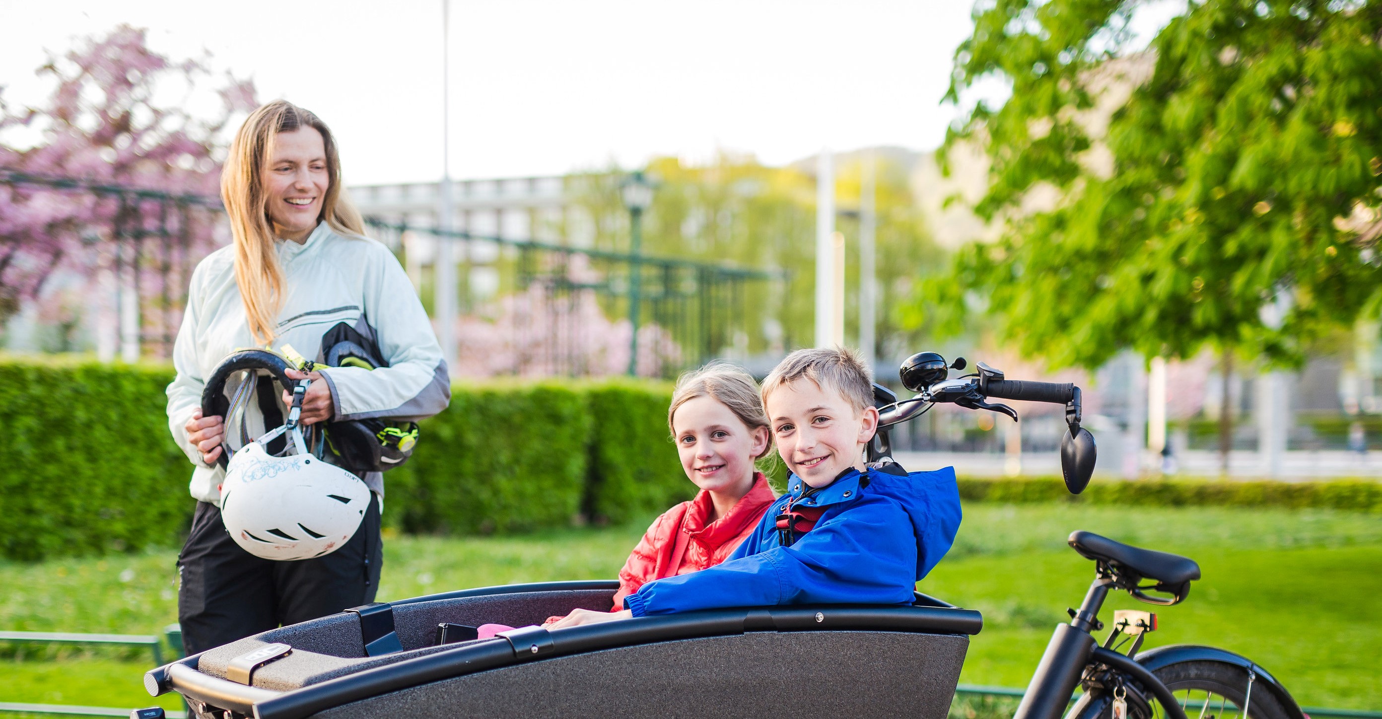 kvinne står ved lastesykkelen sin der det sitter to barn oppi