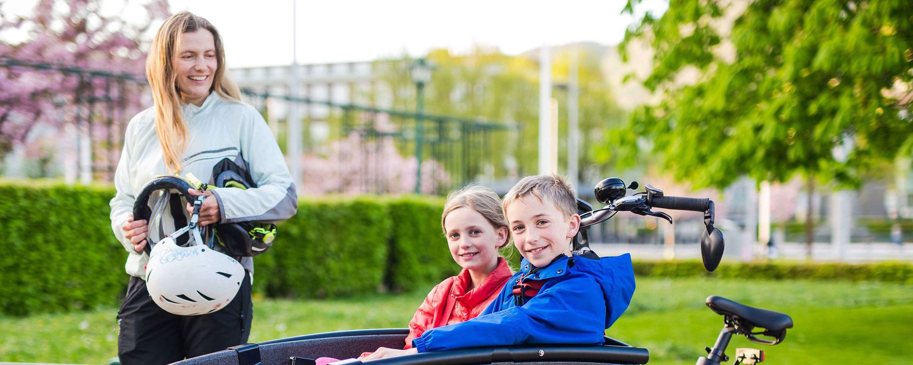 kvinne står ved lastesykkelen sin der det sitter to barn oppi